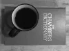 A cup of coffee placed on top of a copy of the Chambers Dictionary, seen from above